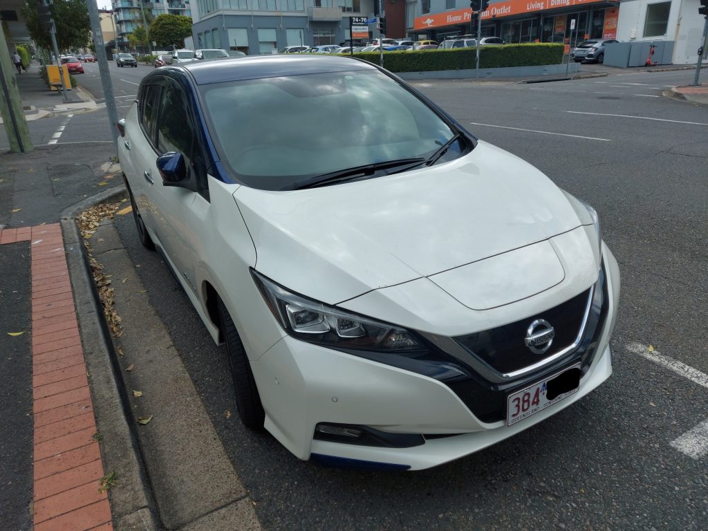 A white Nissan Leaf, parallel parked on a street
