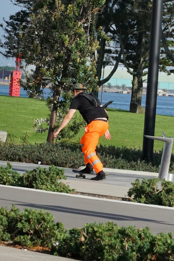 A skateboarder with hi-vis pants and a black shirt pushes along.