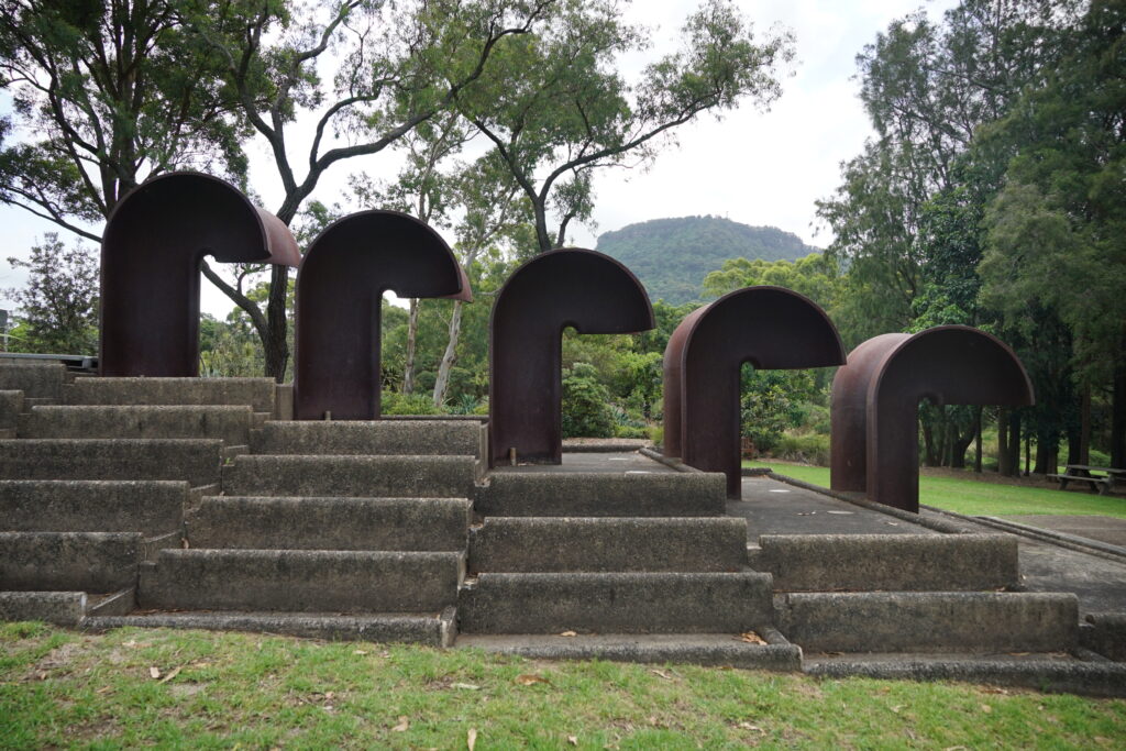 An inactive water feature with 5 steel structures that resemble the letter "r".