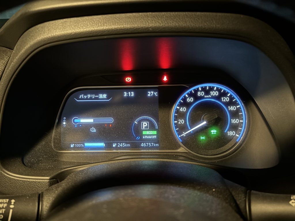 A photo of the digital dash display inside the car. The clock reads 3:13. The temperature reading is 27 degrees Celcius. The battery temperature gauge sits approximately at the halfway point. The battery gauge indicates 100% charge, and an estimated range of 245 kilometres. The odometer reads 46757 kilometres.