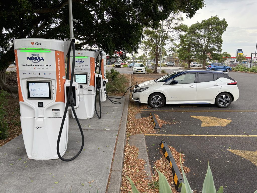 A wide picture of a Nissan Leaf charging in the background, with two other available electric vehicle chargers in the foreground.