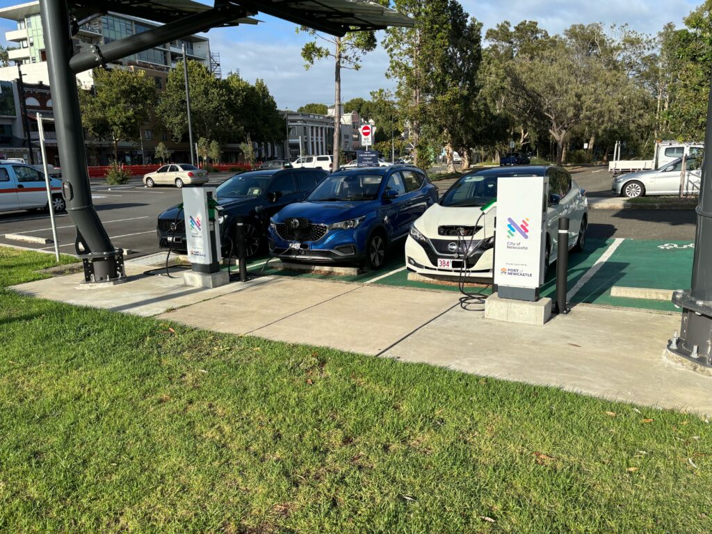 Three electric vehicles parked and charging from two charging stands affixed with the "City of Newcastle" logo.