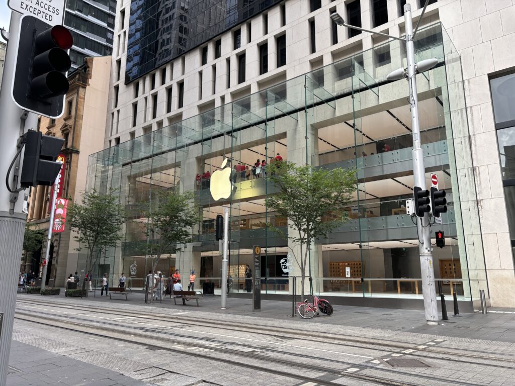 Exterior of the central Sydney Apple Store before opening, with employees dressed in red standing along the outer facing glass.