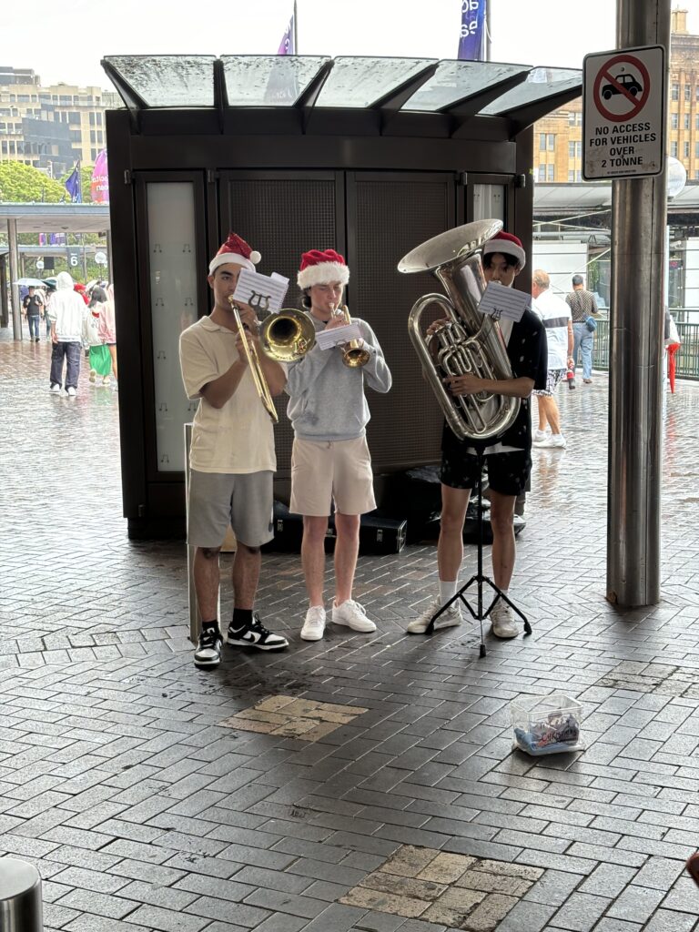 Three buskers with wind instruments playing Christmas songs outside Circular Quay wharf.