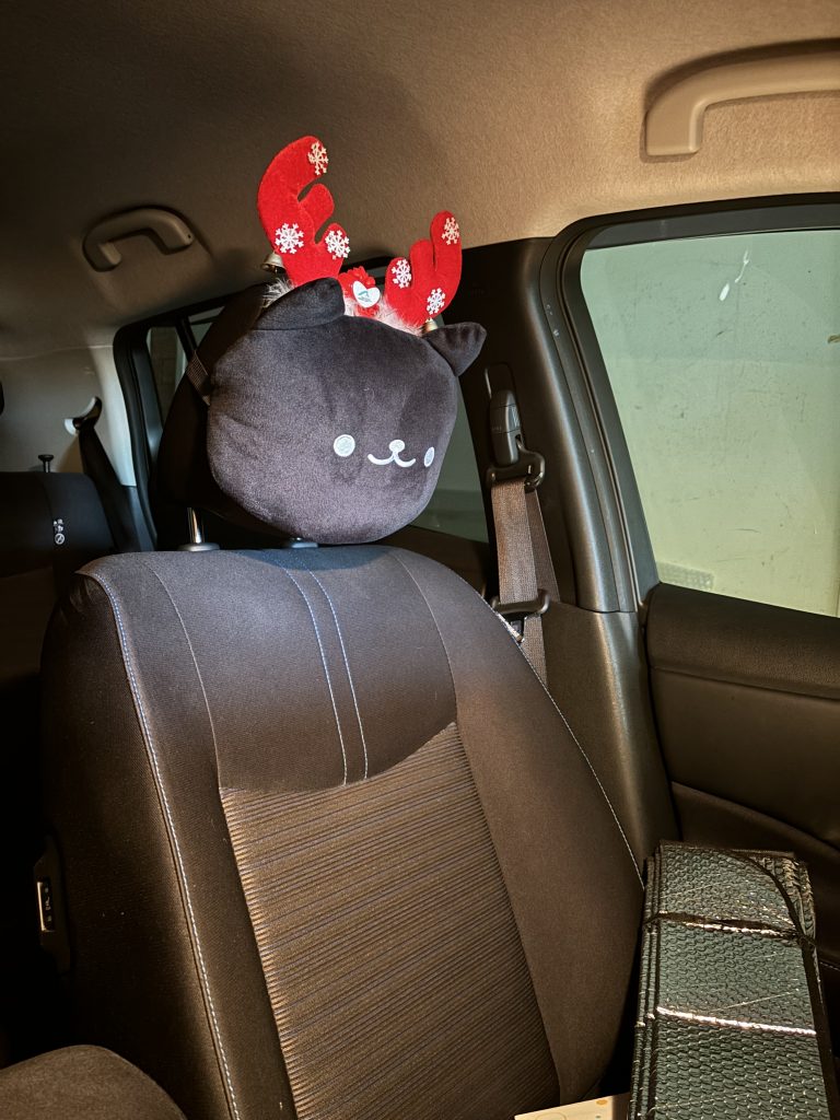 A picture of the passenger seat in a car, with the head rest attached shaped as a cat's head, and Christmas-themed antlers inserted.