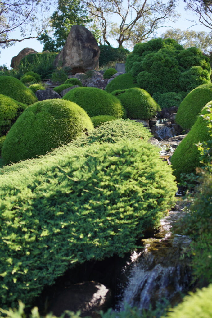 A number of mossy rocks sit against a hill, with water flowing down a stream along the right.