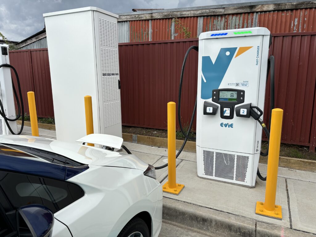 An Evie electric vehicle charger with port 1 in use and connected to a Nissan Leaf; to the left is the power distribution equipment cabinet.