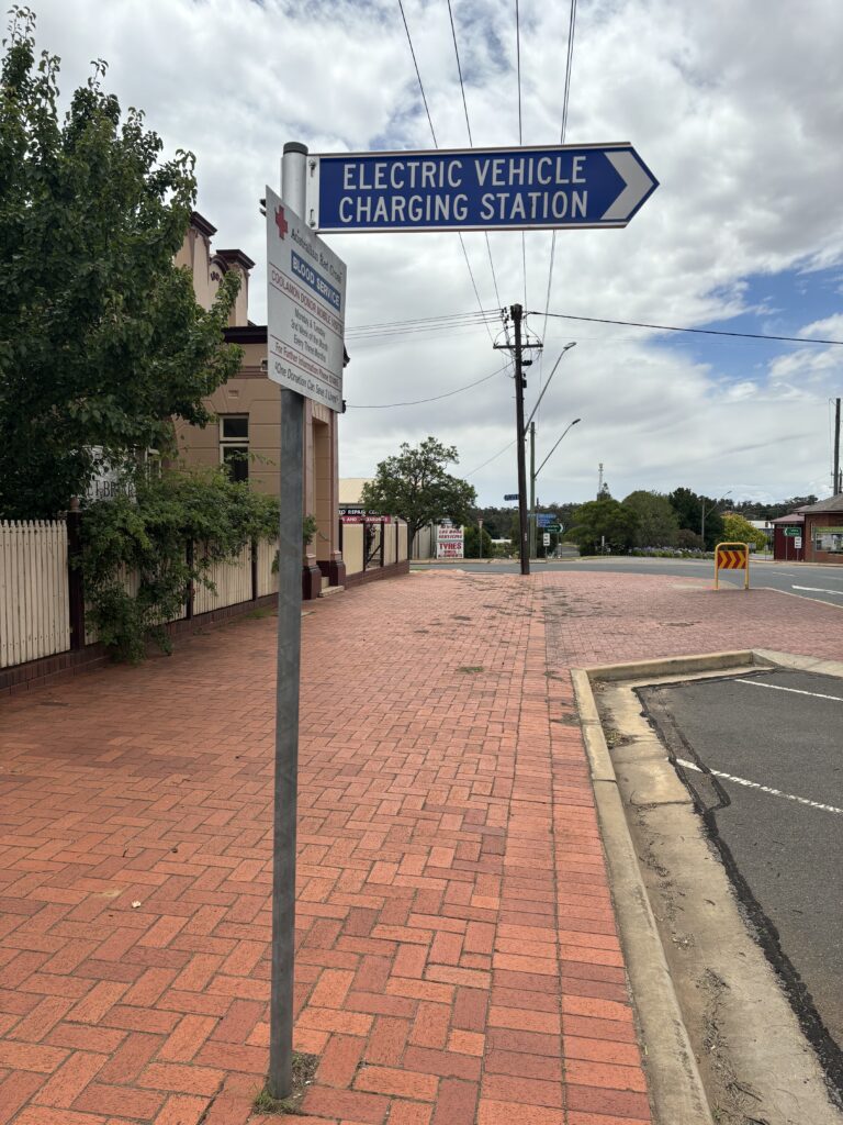 A pole with a blue sign pointing right that reads: "Electric vehicle charging station".